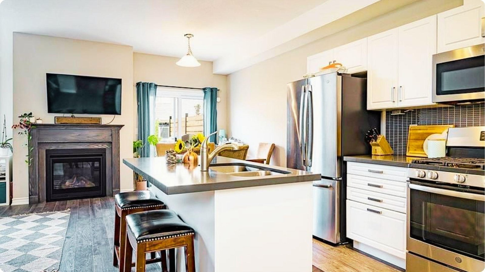 Open-concept kitchen with crisp white shaker cabinets, dark countertops, and a dark oak fireplace mantel.