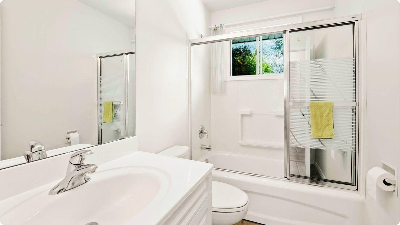 Small, bright bathroom with white walls in semi-gloss sheen, white vanity, and sliding glass shower doors.