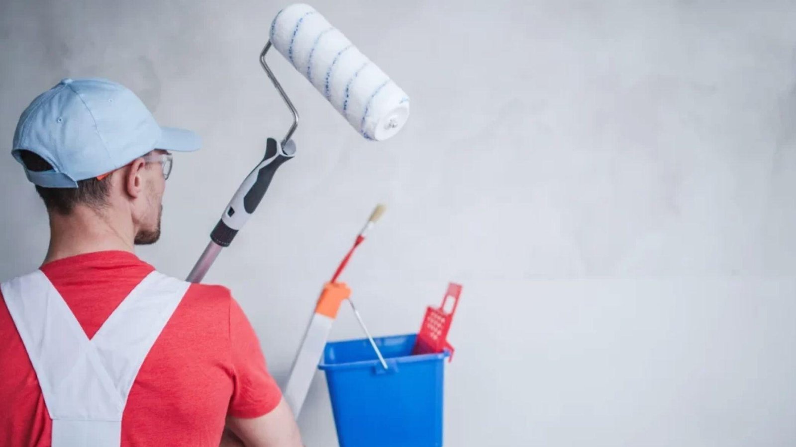 Painter in red shirt holding roller before second coat, showing proper paint drying time between coats