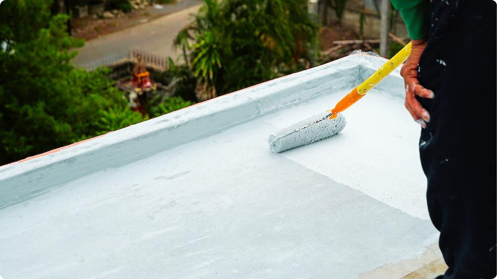 Contractor uses a roller with an extension pole to apply white elastomeric coating over a TPO roof with reinforcing mesh.