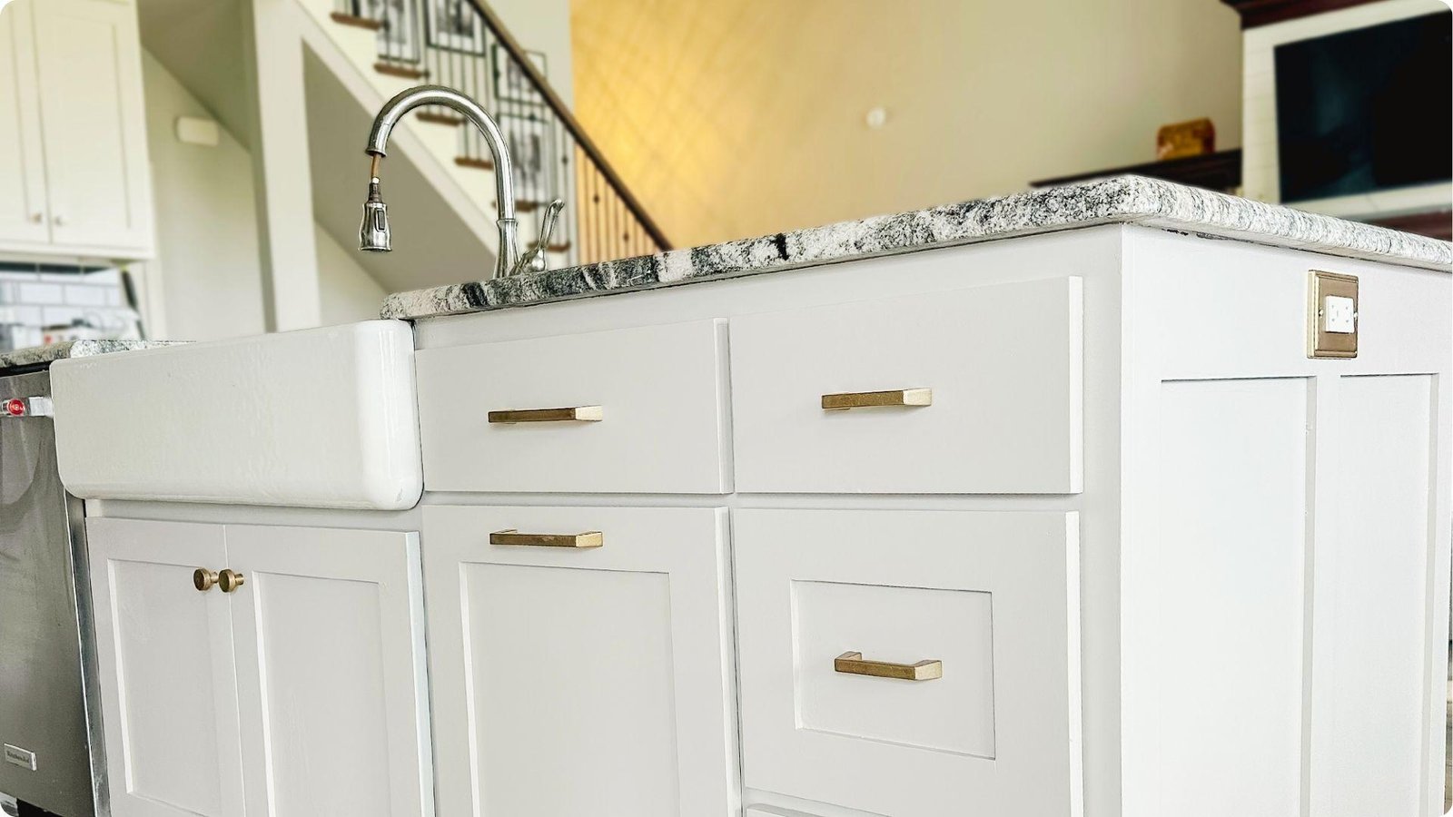 Clean white painted kitchen island cabinets with gold handles and a farmhouse sink after cleaning.