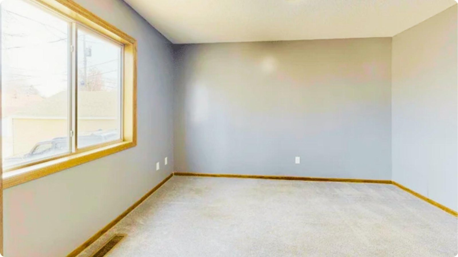 Bright empty room with gray walls, carpet flooring, and large window showing finished paint job.