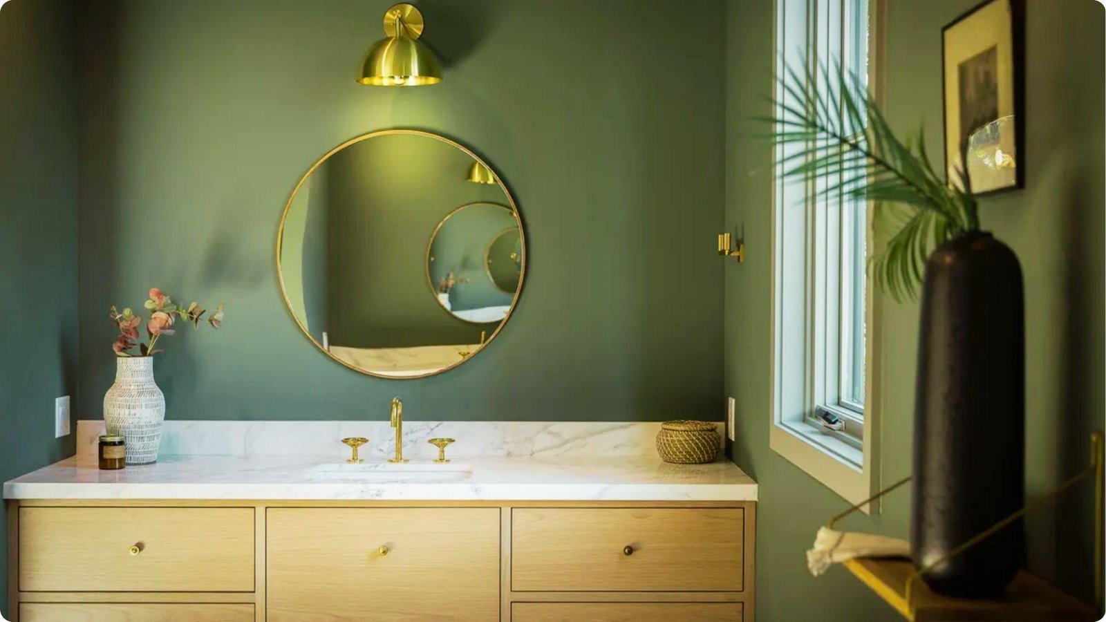 Stylish bathroom with deep sage green walls in satin sheen, paired with brass fixtures and a round mirror.