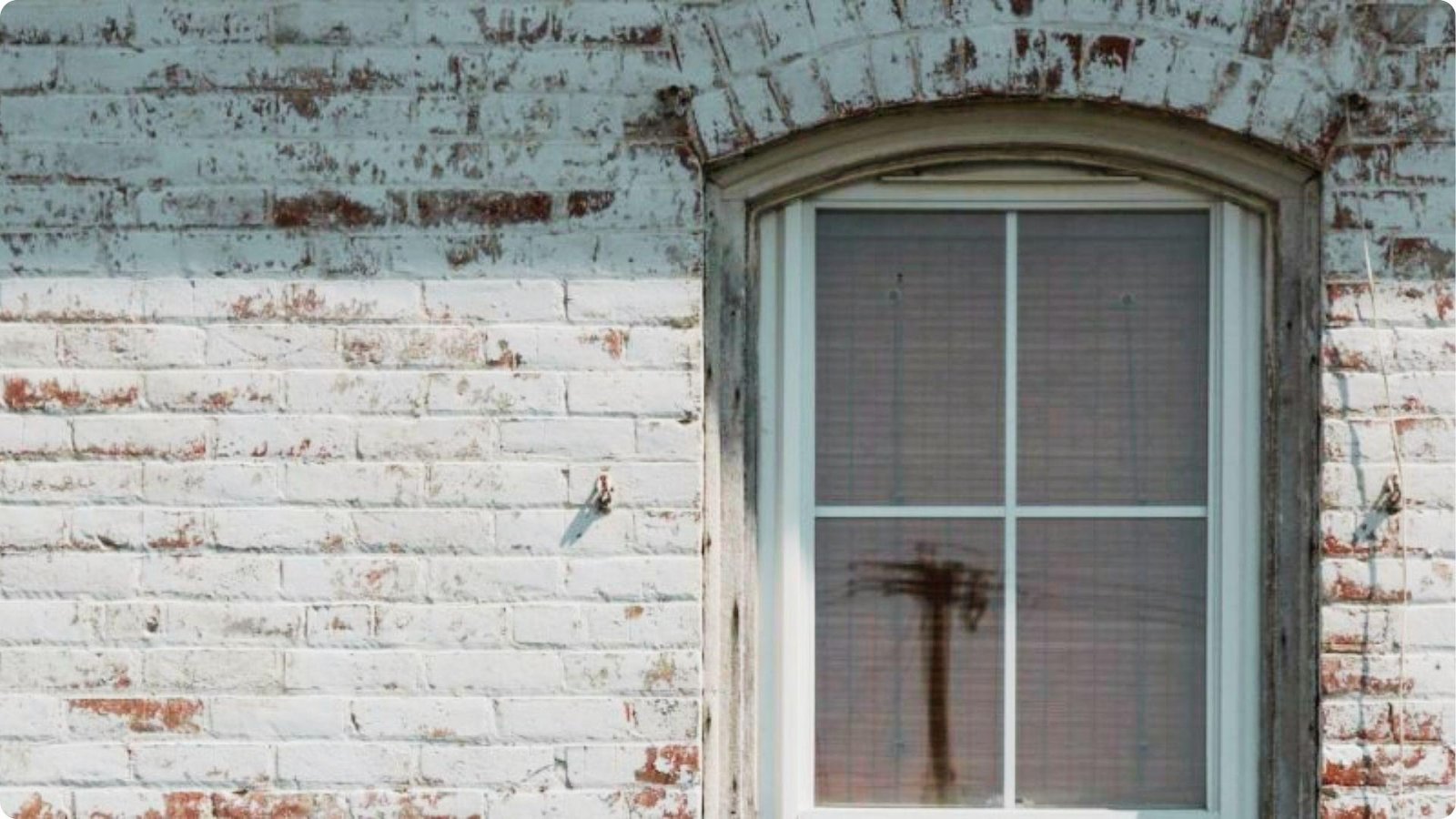 Close-up of an arched window set in a brick wall partially covered in distressed whitewash.