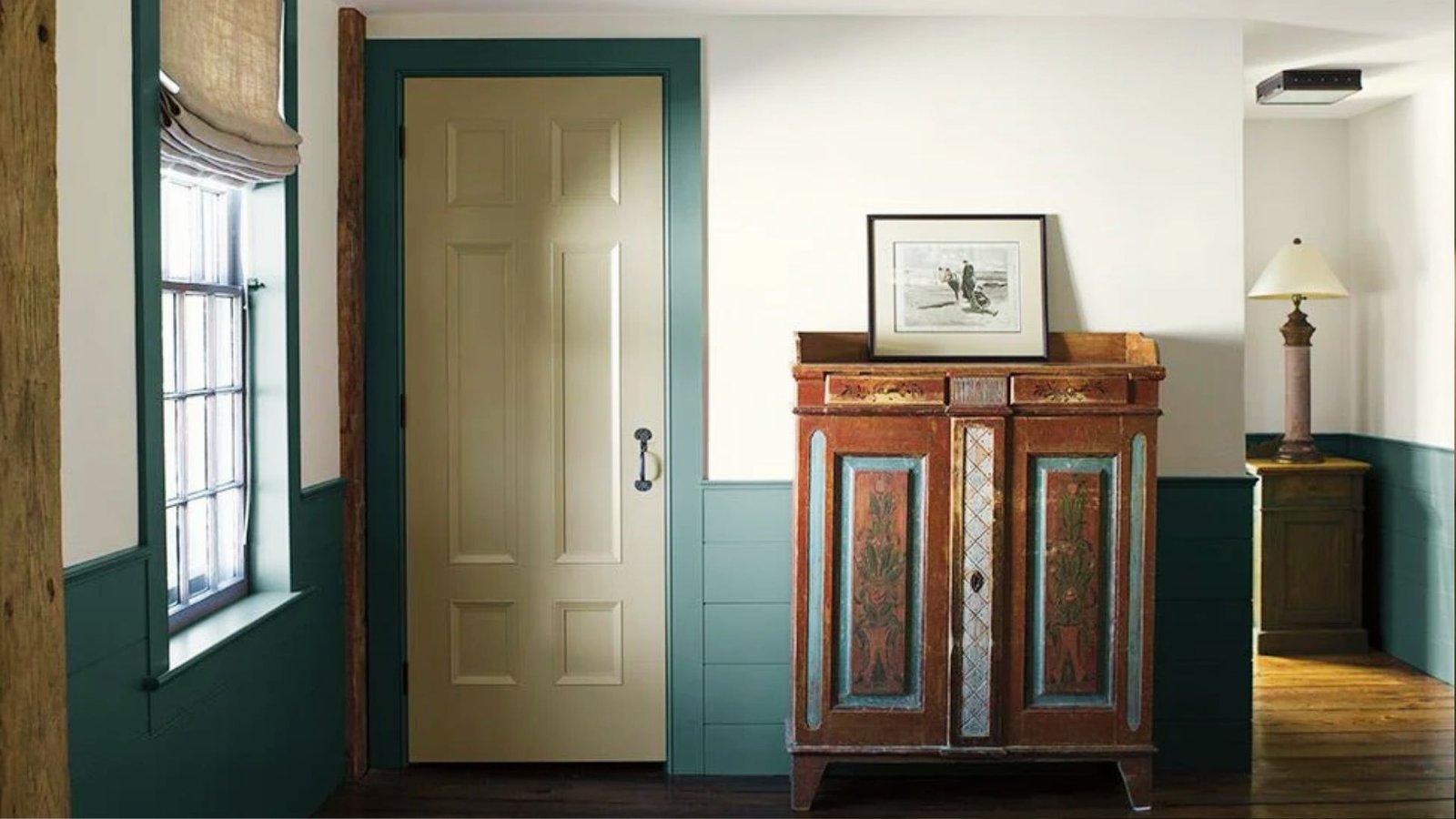 Entryway with bold teal trim paint on door frame and wainscoting contrasting cream walls and antique cabinet