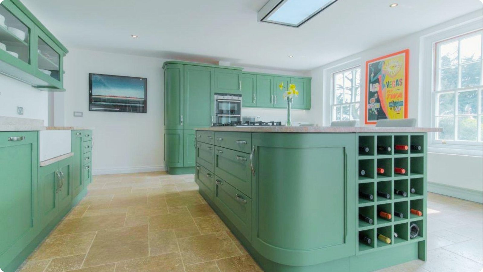 Bright farmhouse kitchen featuring mid-tone green painted cabinets and a large island with built-in wine storage.