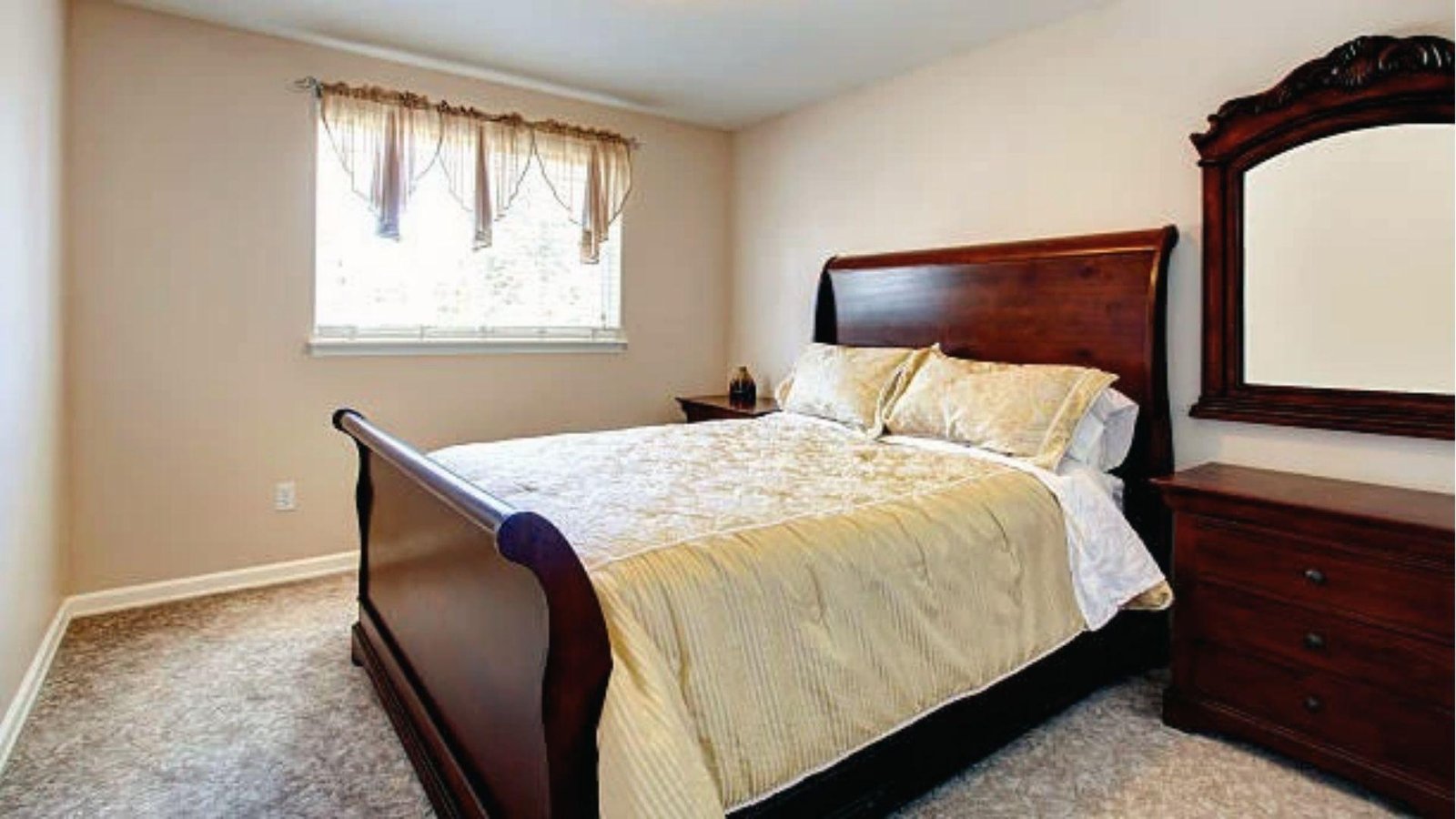 Cherry wood bedroom suite with gold bedding, beige carpet, large ornate mirror frame.