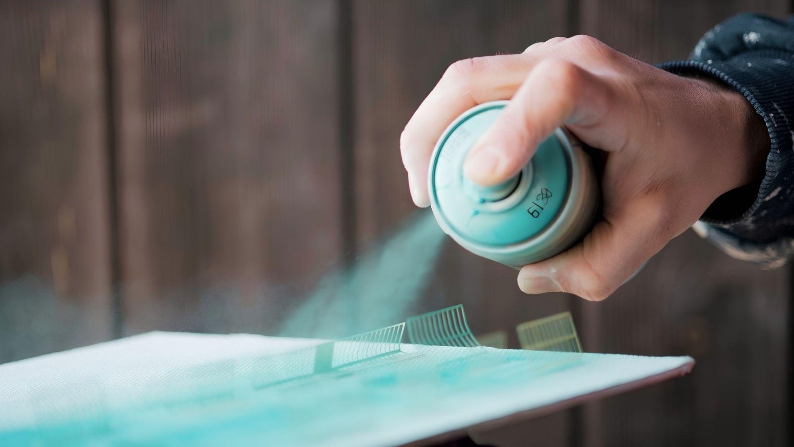 Hand spraying light blue paint on surface, showing spray paint needs proper drying time between coats