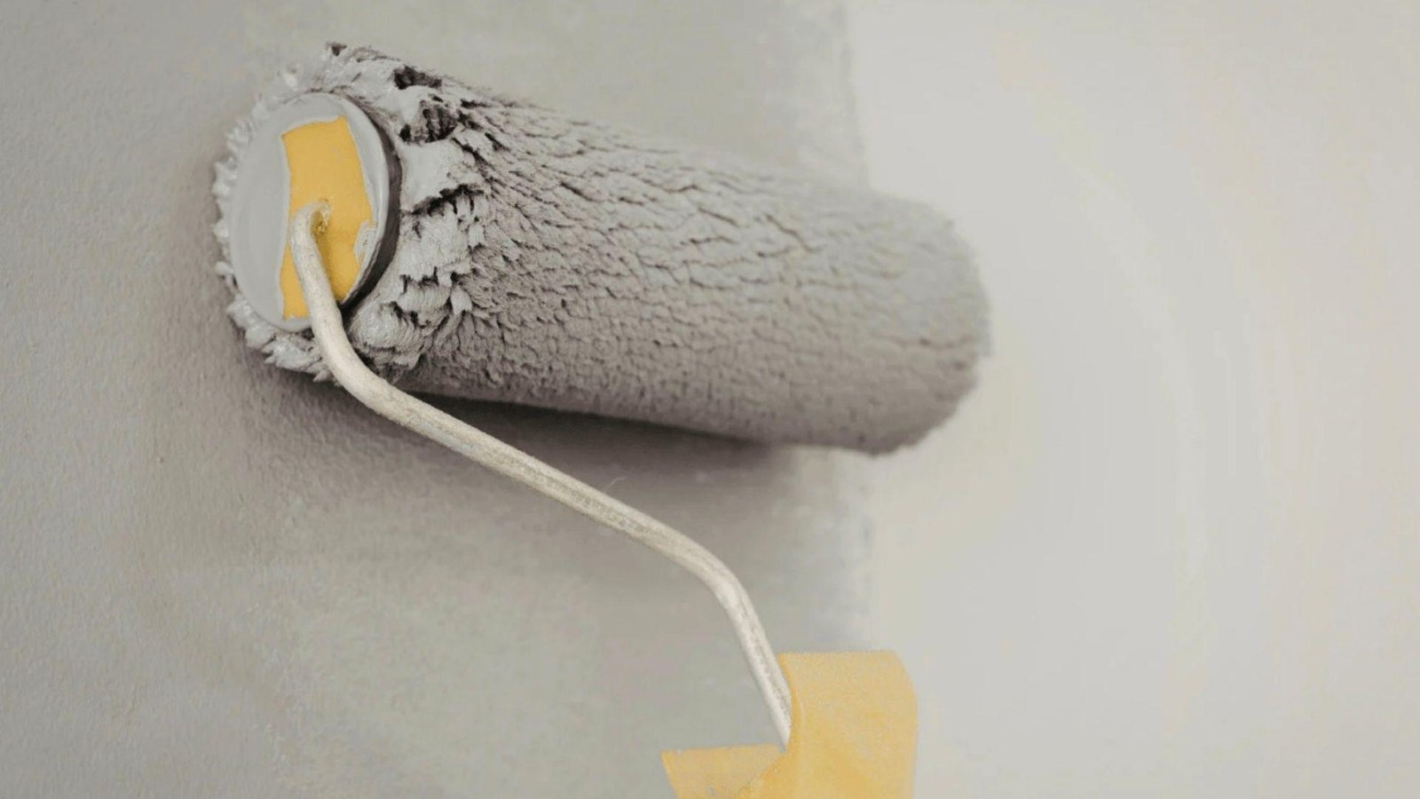 Paint roller applying gray paint to wall, demonstrating even coverage after first coat dries completely