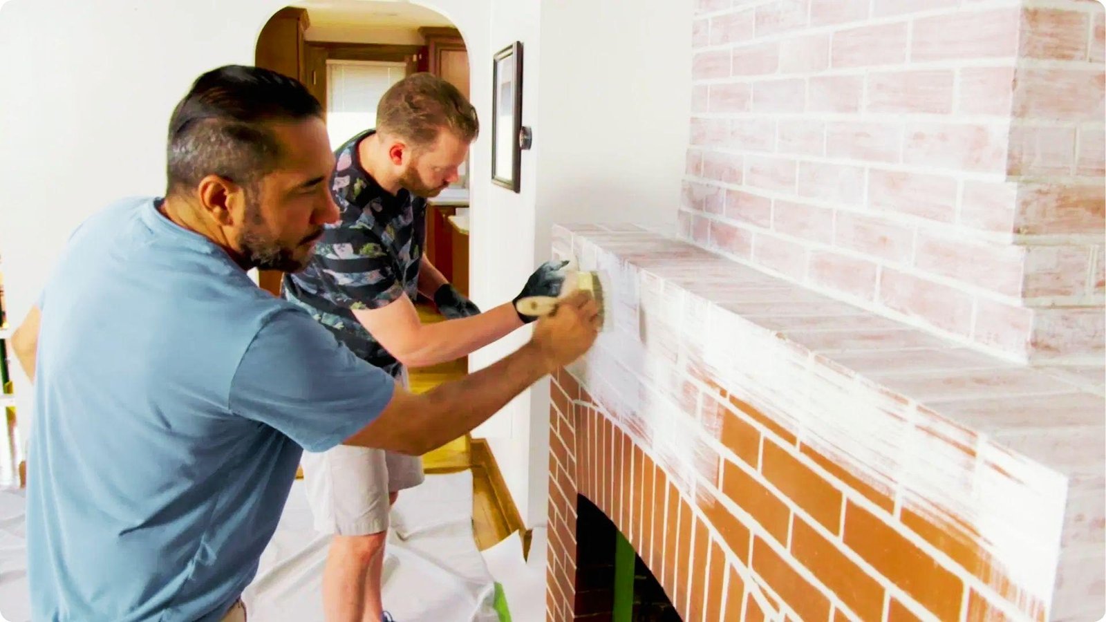 Two men work together to brush whitewash onto a brick fireplace mantel.