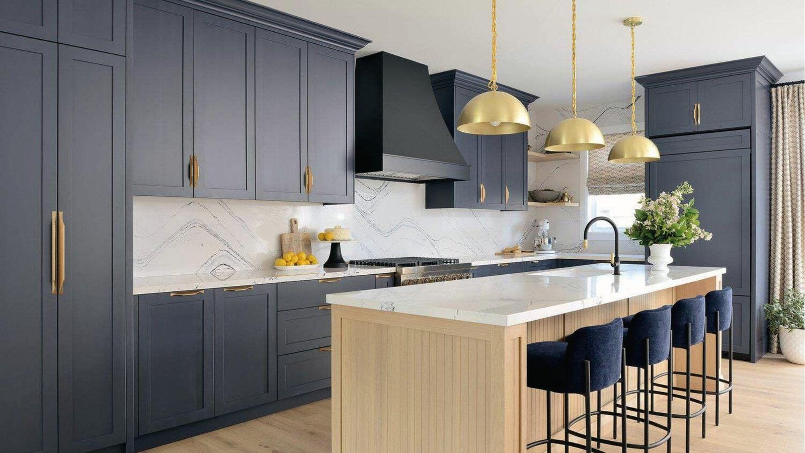 Navy blue cabinets with white marble counters, gold hardware, light wood island, warm contrast scheme