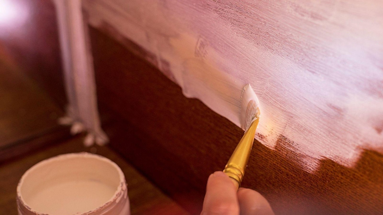 Brushing white paint onto dark wood furniture, waiting for paint to dry between coats prevents streaks and peeling