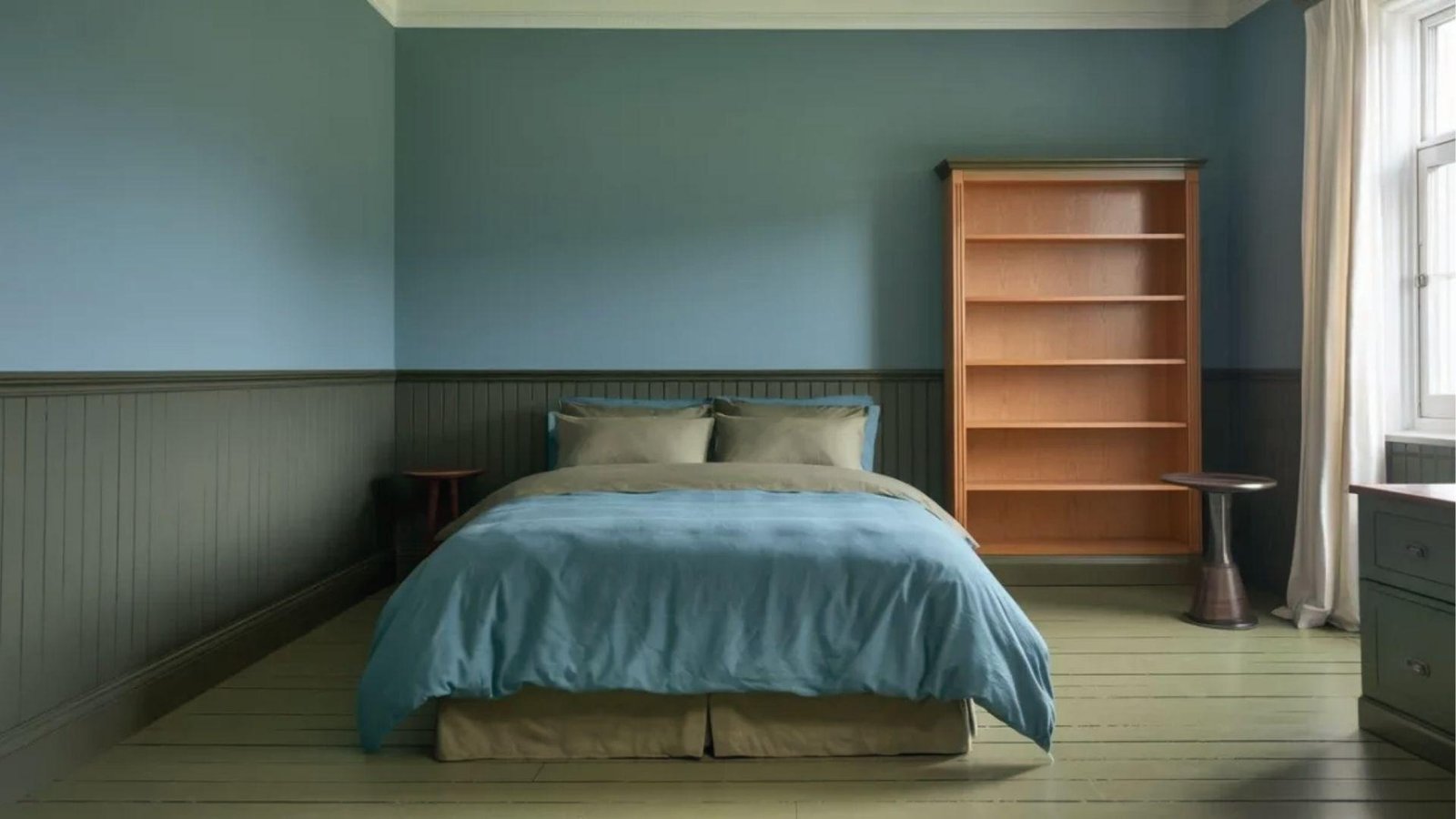 Bedroom with Dark Teal and Green wainscoting below behind bed and wood bookshelf.