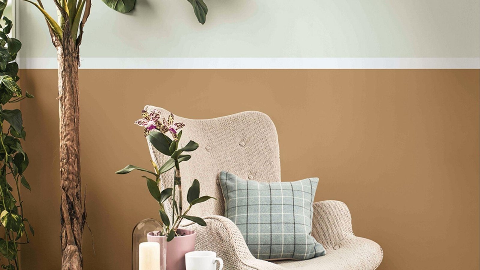Cozy corner with White and Tan horizontal two tone wall behind armchair, orchid, and candle.