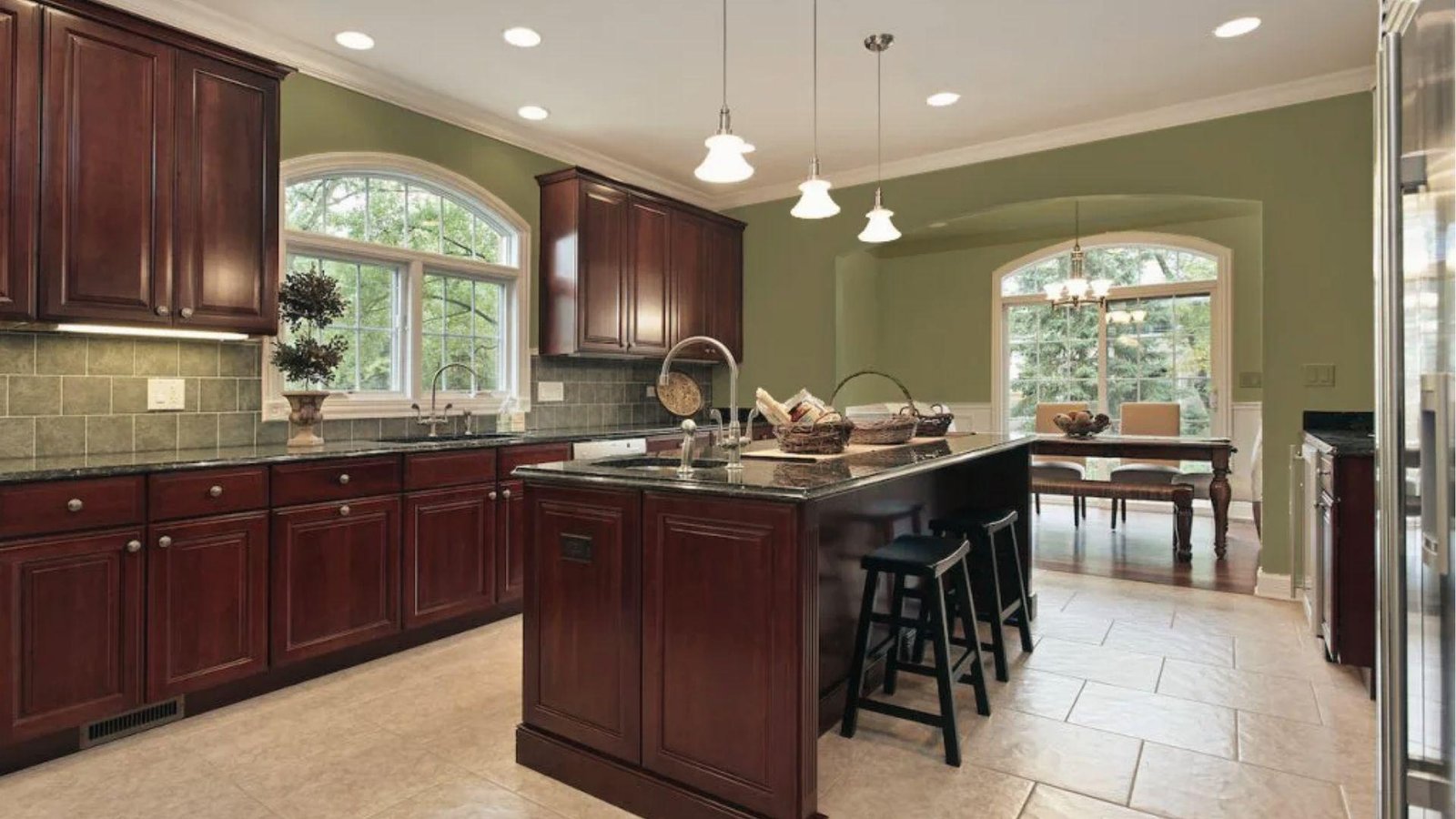 Rich cherry wood cabinets paired with sage green walls, black granite, traditional dark kitchen palette
