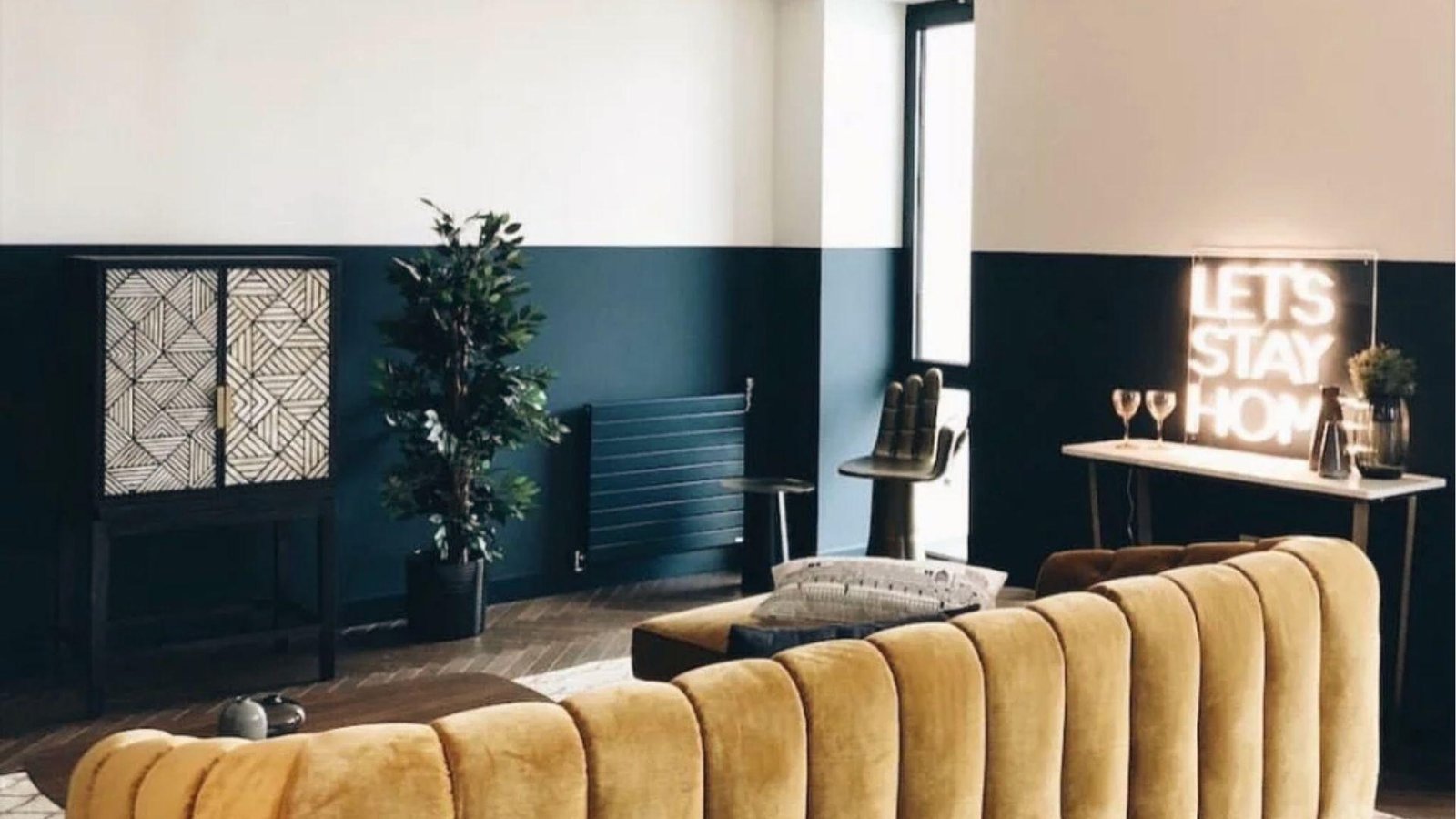 Stylish living space with deep teal lower half and crisp white upper two tone wall near neon sign.