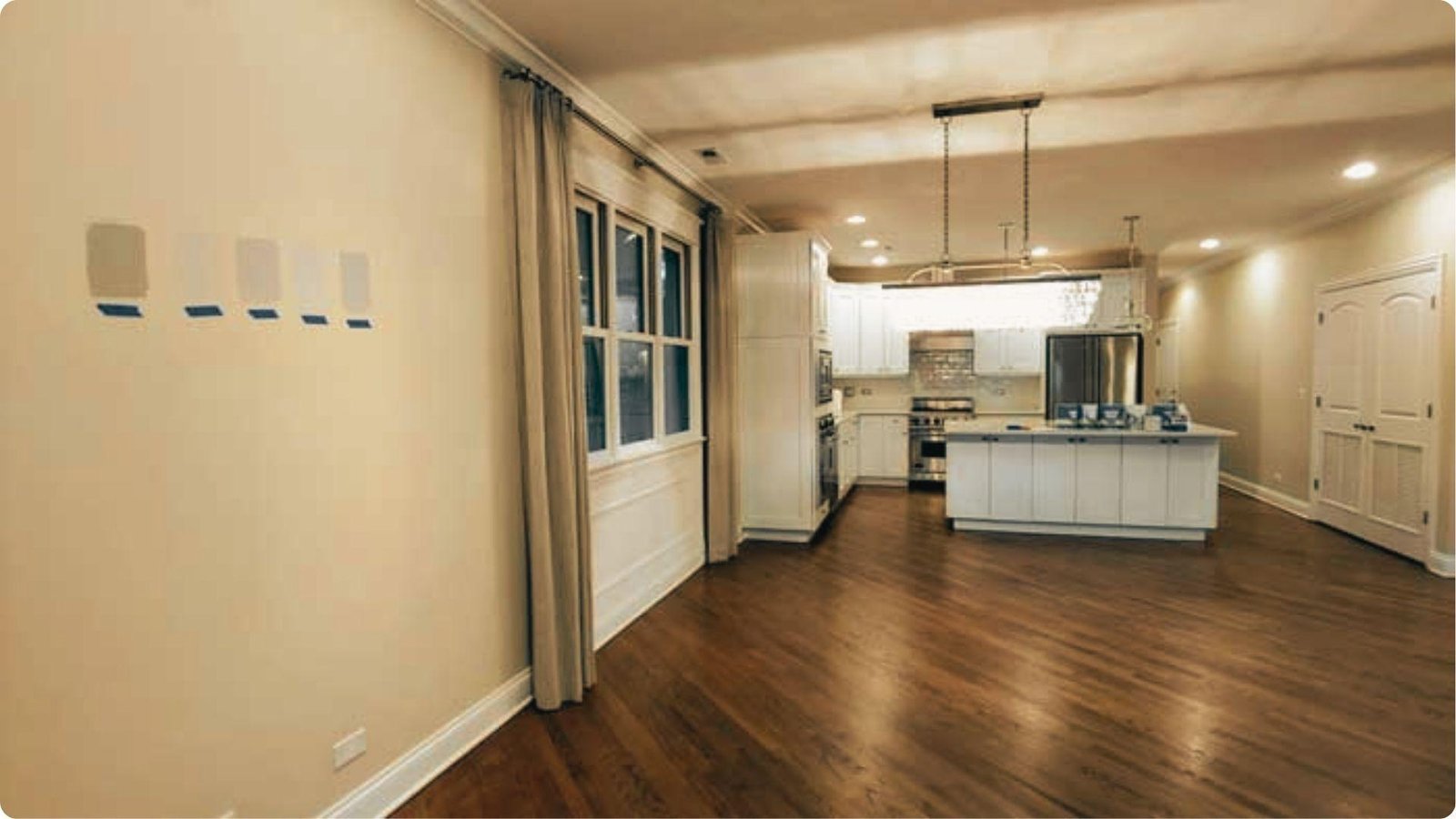A modern kitchen with wood flooring shows paint swatches taped to the wall for color testing.
