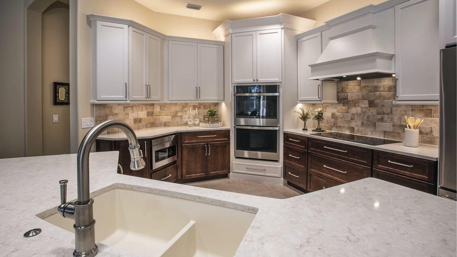 Two-tone kitchen with dark walnut lowers, white uppers, stone tile backsplash, balanced warm contrast