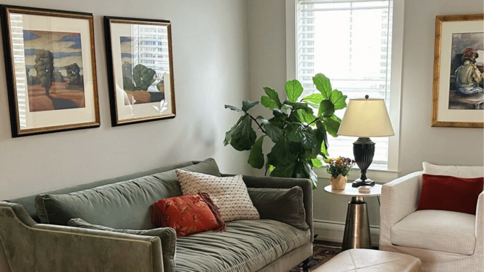 Cozy living room with muted green sofa, art frames and warm lighting against light grey walls.