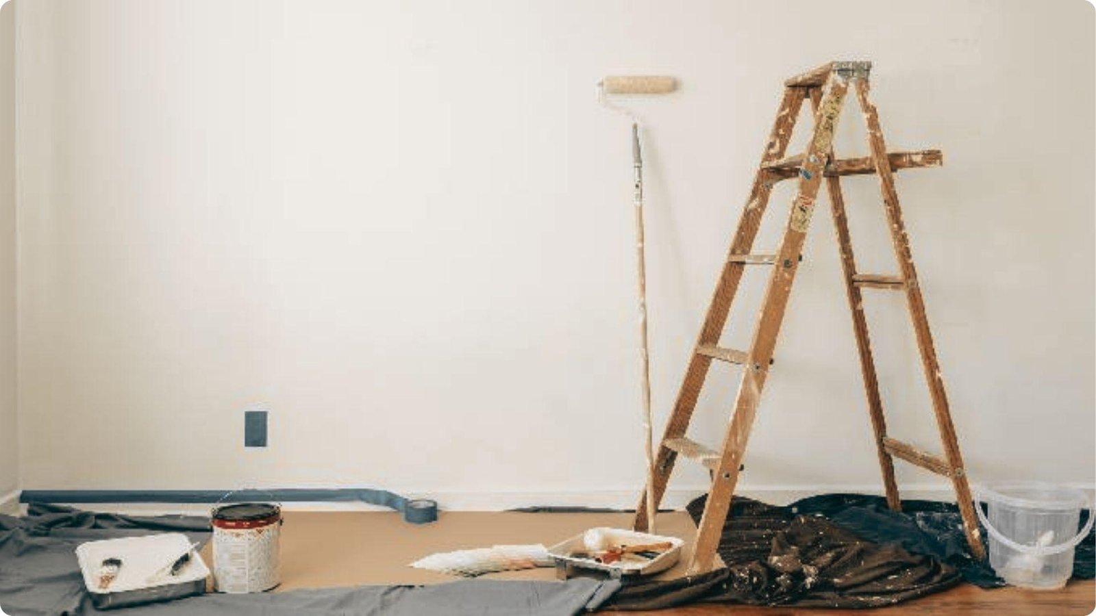 An empty room with painting supplies, a wooden ladder, and drop cloths prepared for work.