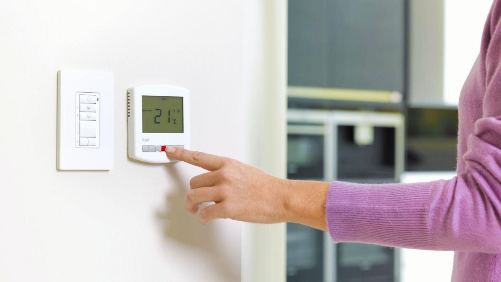 Person adjusting thermostat to 21°C, since room temperature impacts how long paint takes to dry between coats