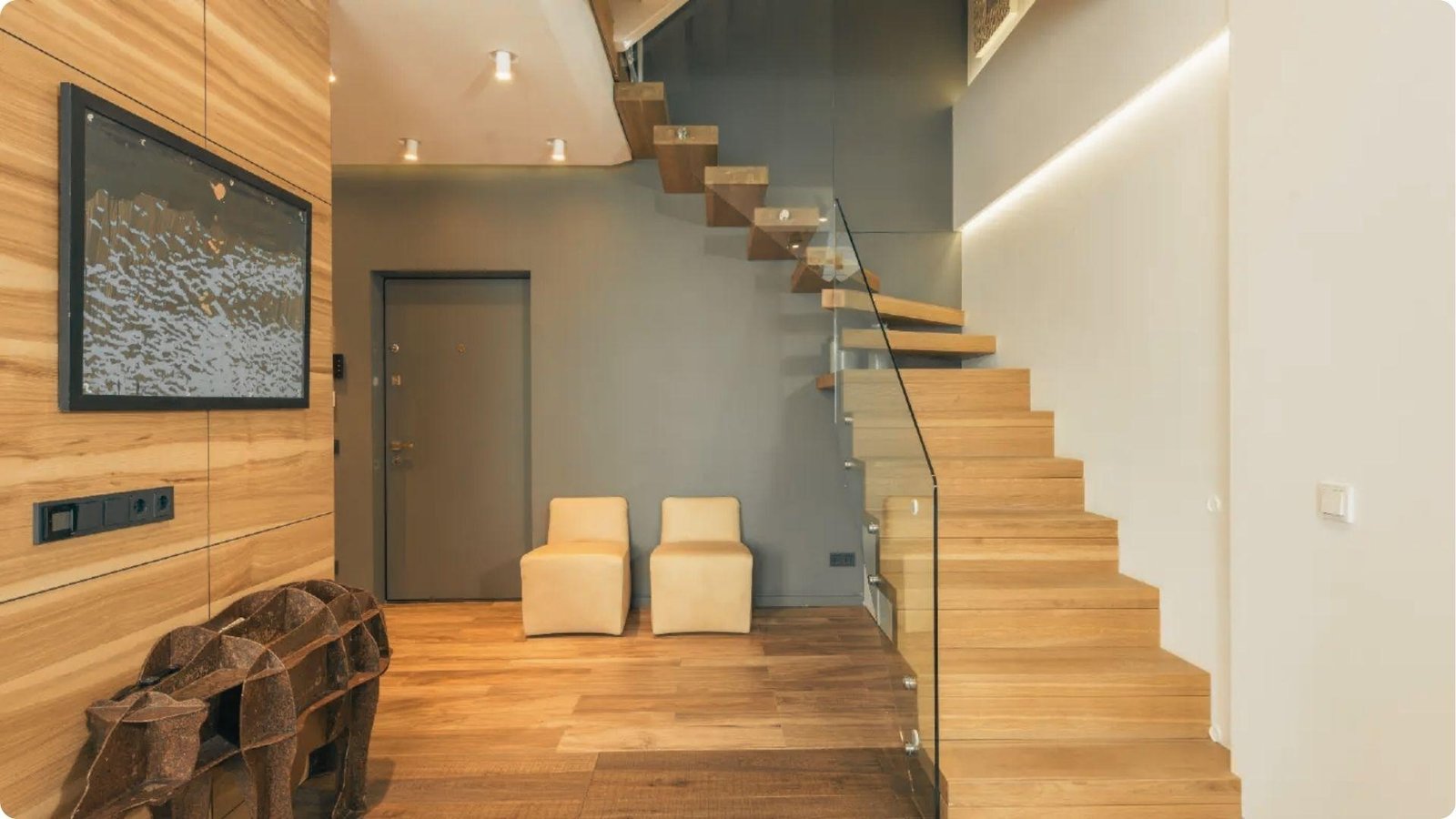 Contemporary home entry featuring grey painted accent walls, wood paneling, and a floating wooden staircase with glass railing.