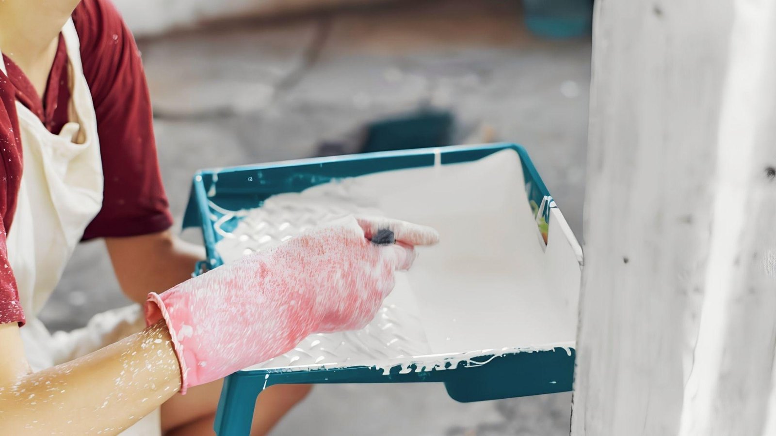 Person in gloves loading roller with white paint, prep work before applying second coat after drying